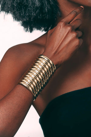 Close up of a woman wearing the Gold Ndebele Cuff and raising her arm towards her face
